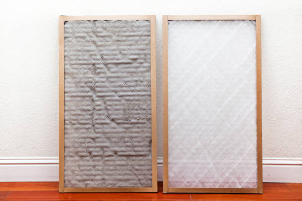A dirty air filter stands up against a wall next to a clean air filter.