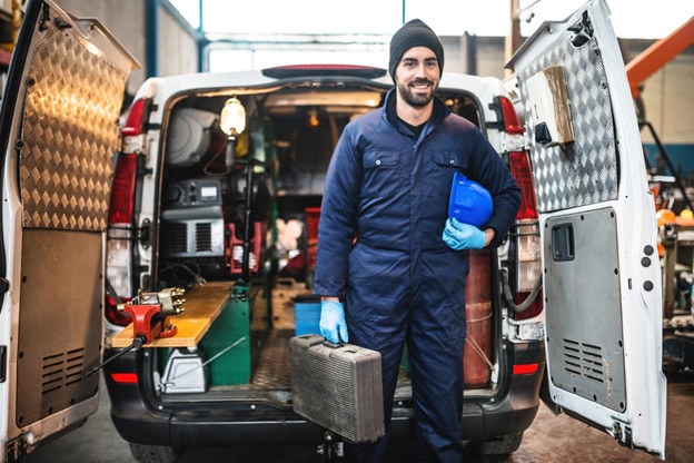 An HVAC technician holding his toolbox by a company van