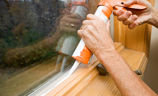 A person using caulk to seal a draft in a window