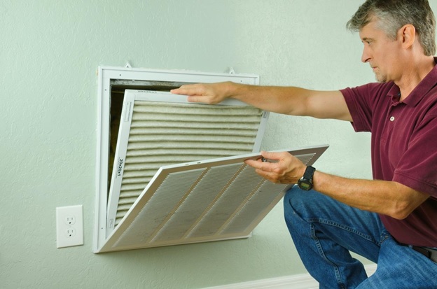 A man in a polo shirt removing an HVAC filter from his vent