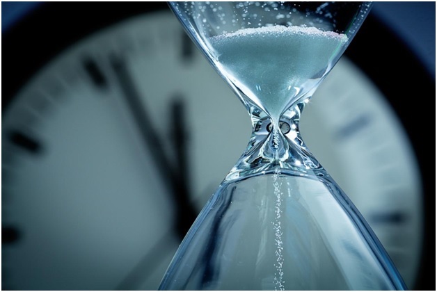 An hourglass in motion with a clock in the background
