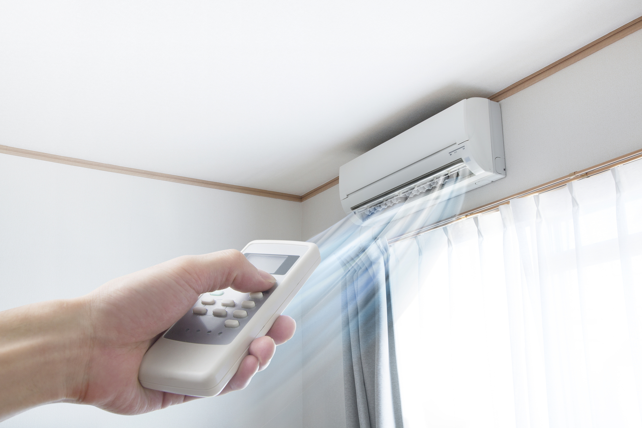 A woman’s hand pointing a remote at a ductless AC unit mounted on a wall