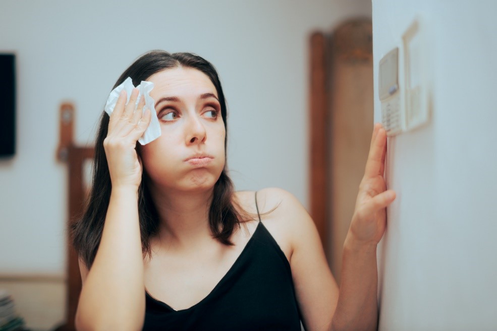A woman wiping sweat off her brow while looking at the thermostat to see if the AC is working