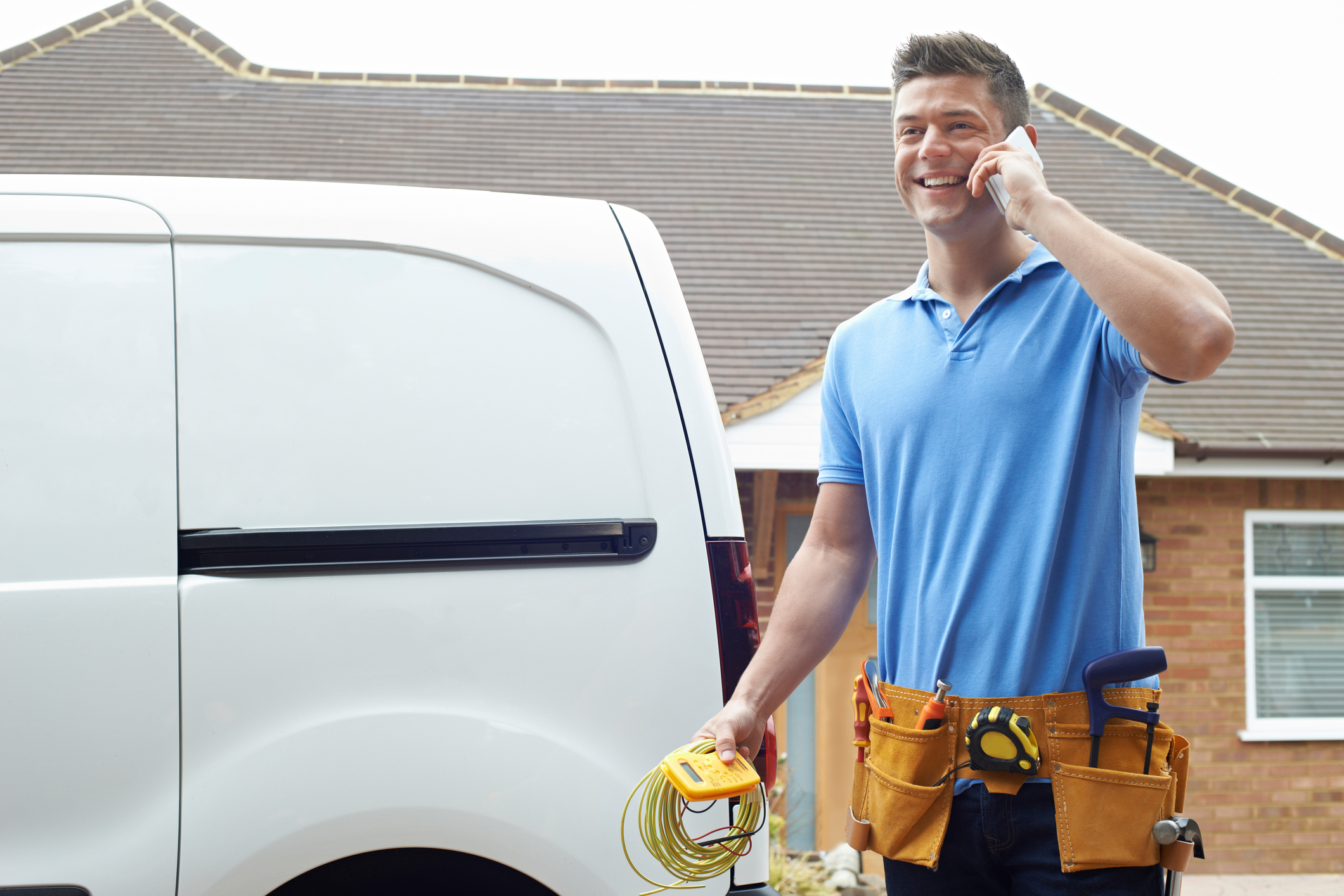 HVAC professional on the phone with toolbelt and work van