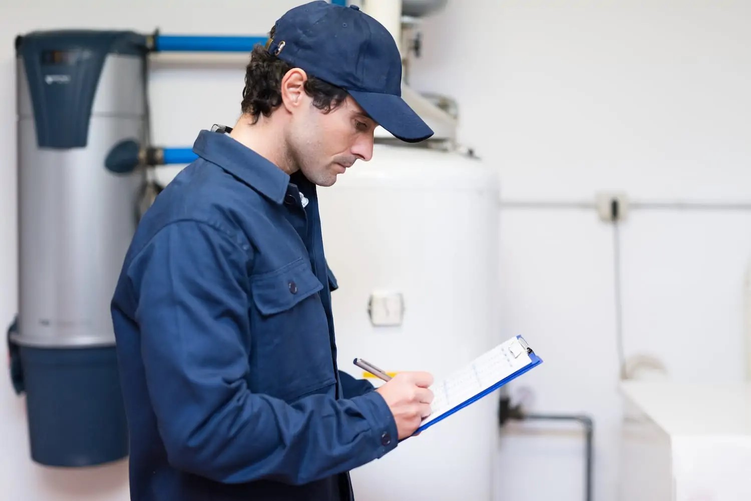 A plumber standing in front of a newly installed water heater with a clipboard