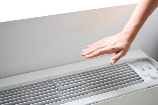 A woman’s hand over the vent of a cooling unit, feeling the temperature